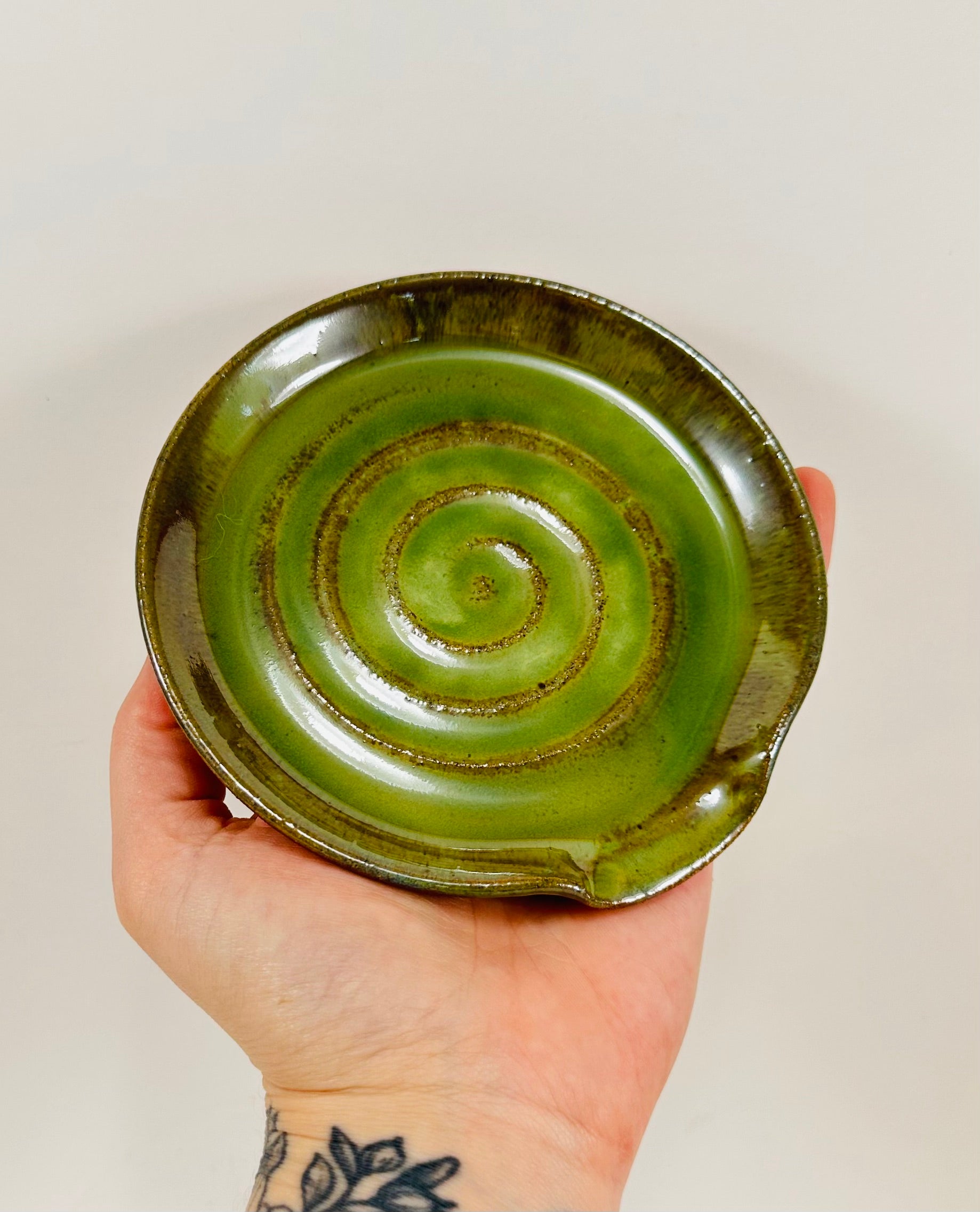 A handmade ceramic spoon rest in a beautiful green glaze on red clay.