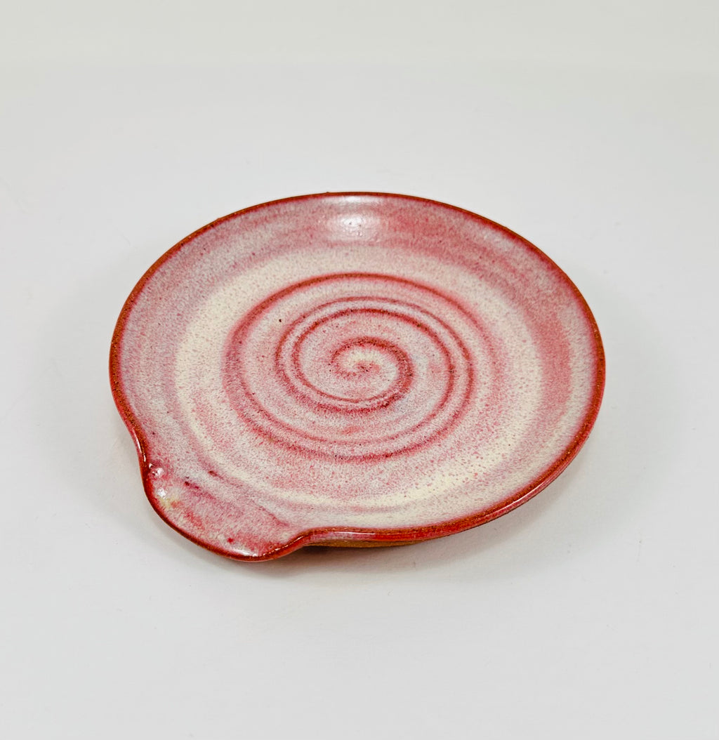 A handmade ceramic spoon rest in a beautiful pink glaze on red clay.