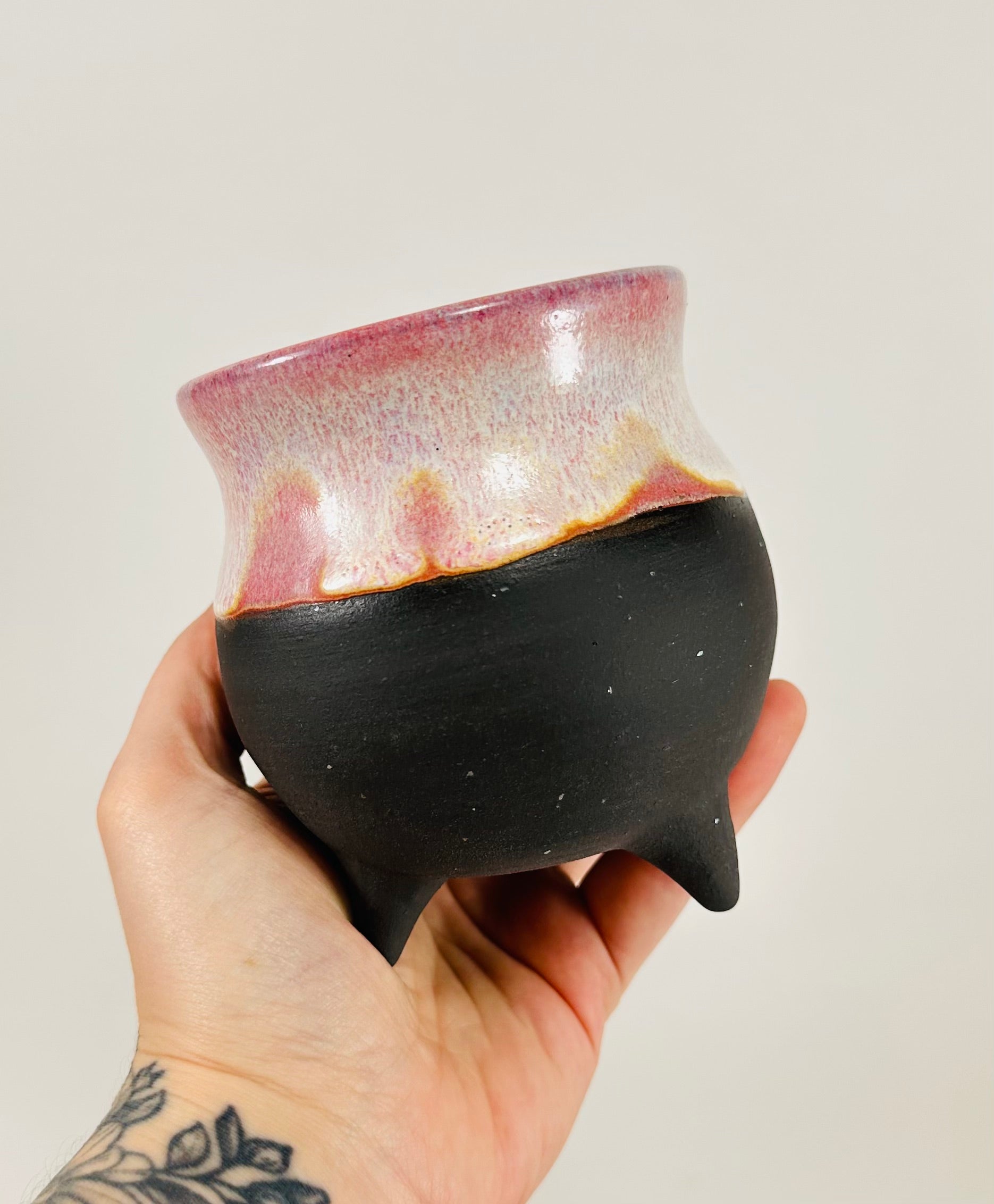 A handmade ceramic cauldron in pink and black glaze.