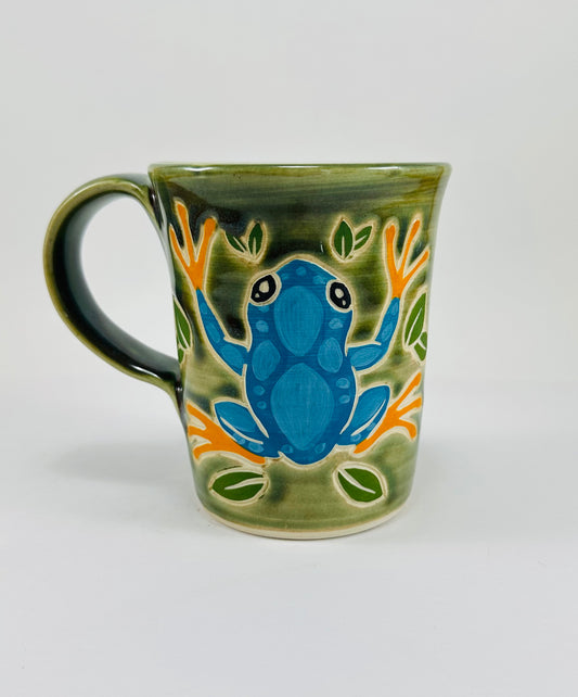 A handmade ceramic mug with a beautiful green glaze and an illustration of a blue frog.