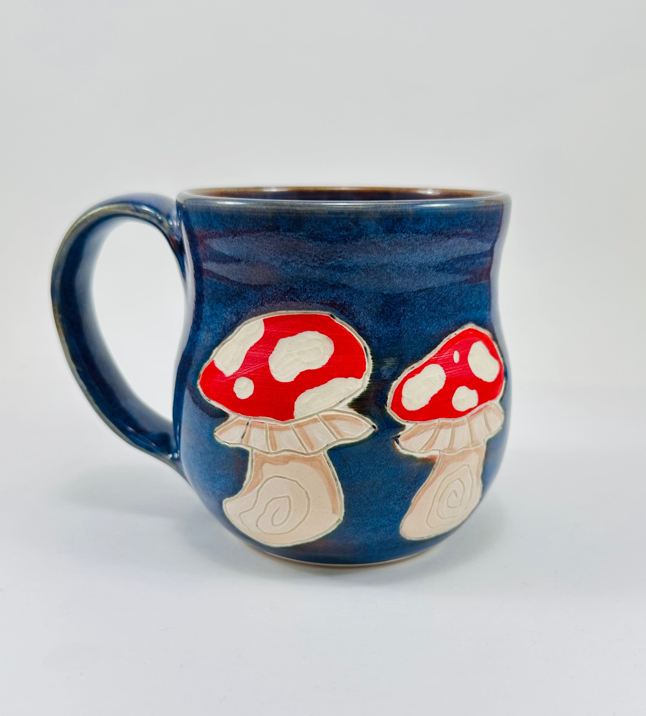 Handmade ceramic mug with mushroom illustrations on it and a beautiful blue glaze.