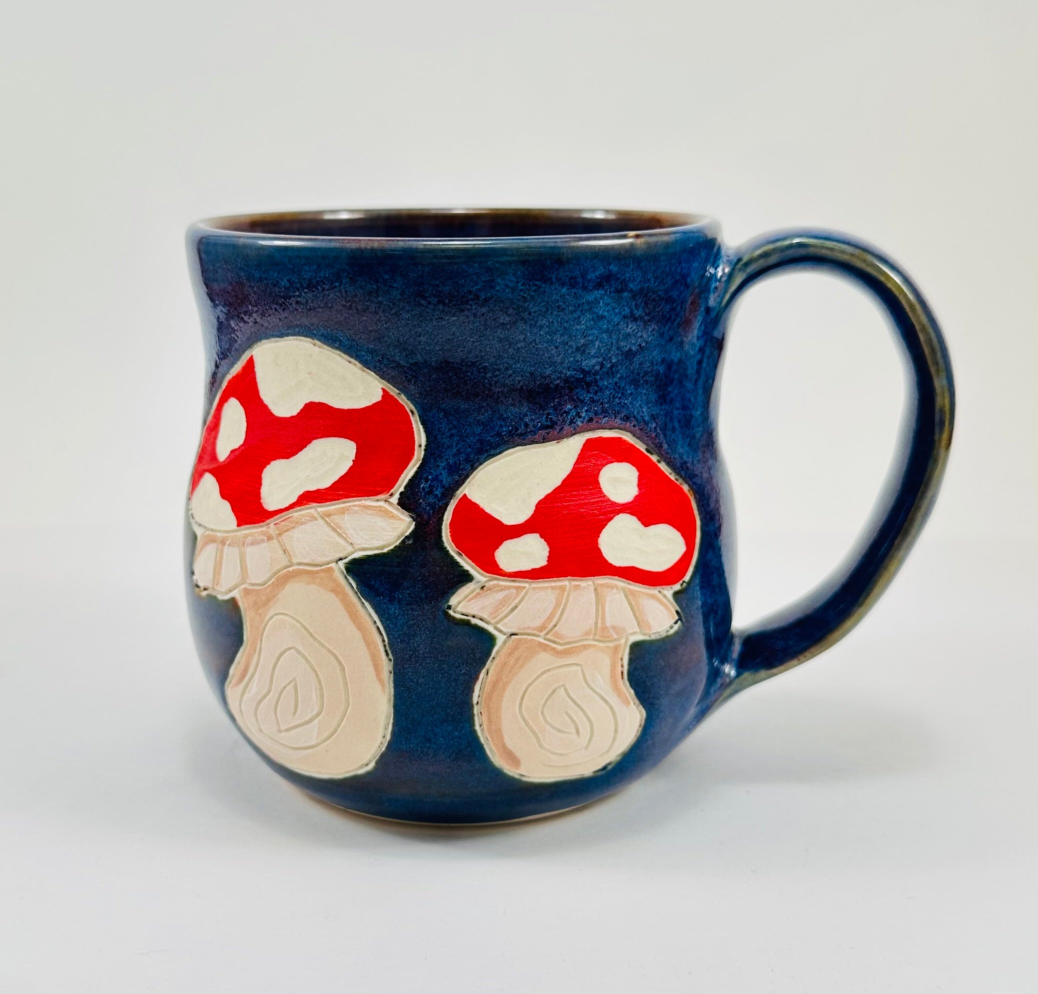 Handmade ceramic mug with mushroom illustrations on it and a beautiful blue glaze.