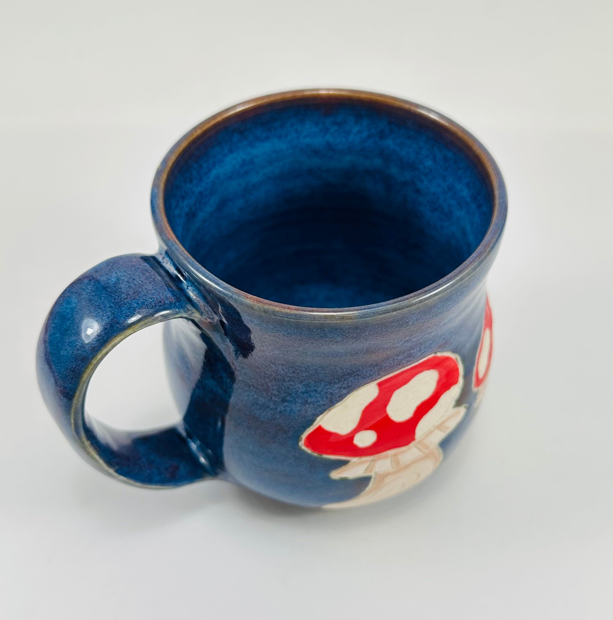 Handmade ceramic mug with mushroom illustrations on it and a beautiful blue glaze.