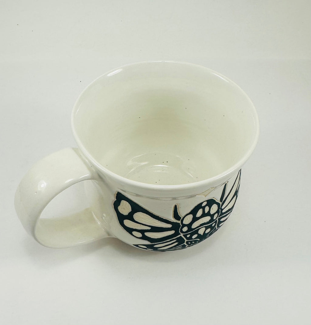 A handmade ceramic mug in a beautiful white glaze with a cicada illustration on it.
