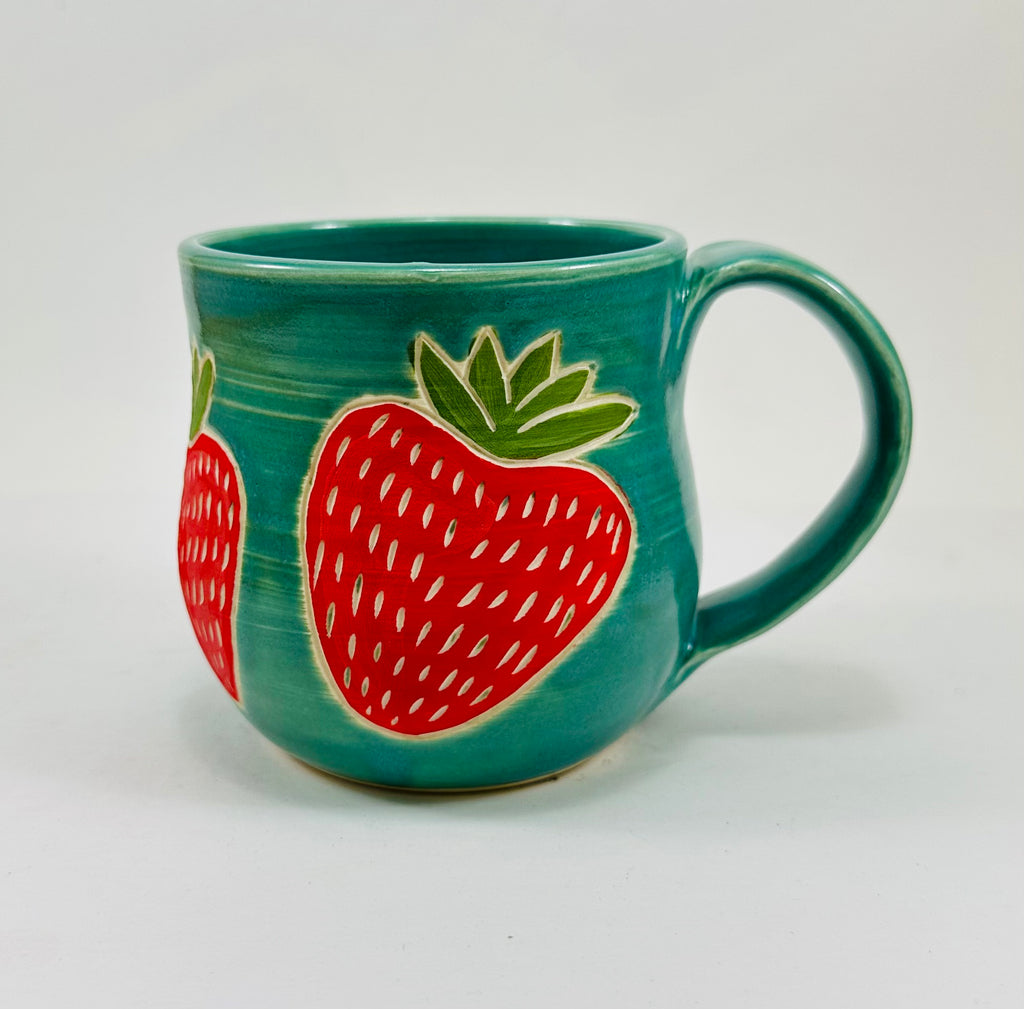 handmade ceramic mug in a beautiful blue/green glaze and illustrations of strawberries on it