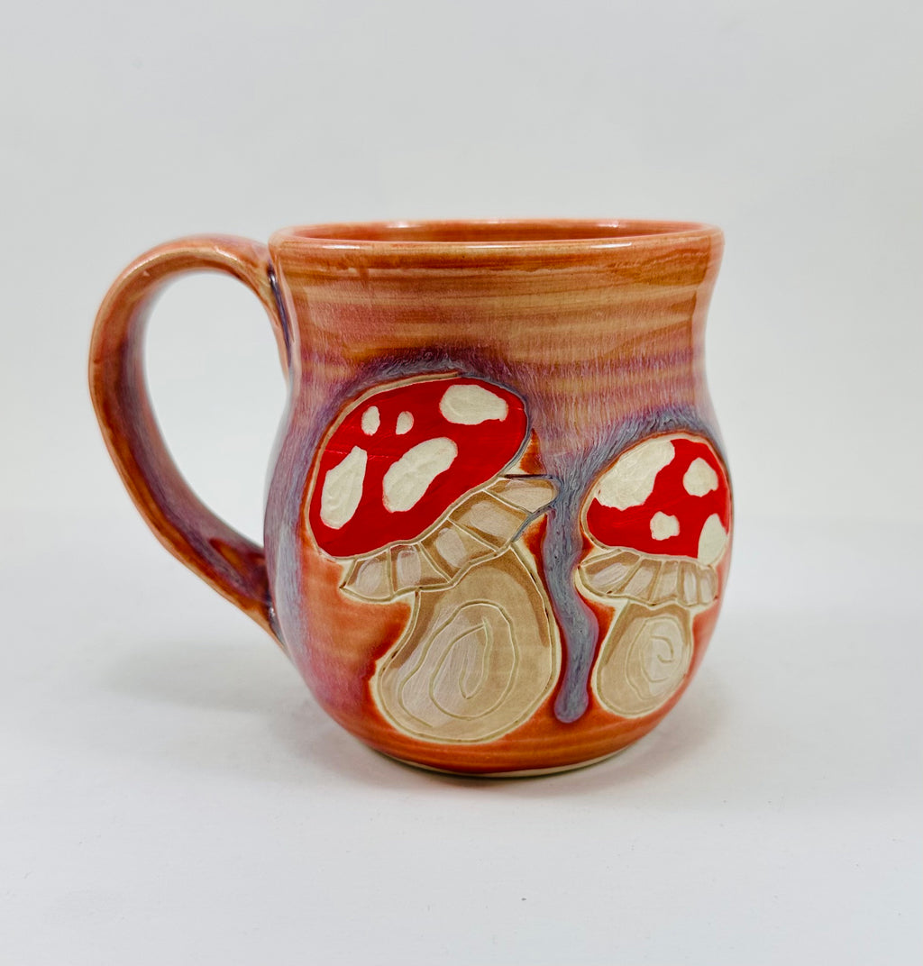 handmade ceramic mug in a beautiful peachy glaze with mushroom illustrations on it.