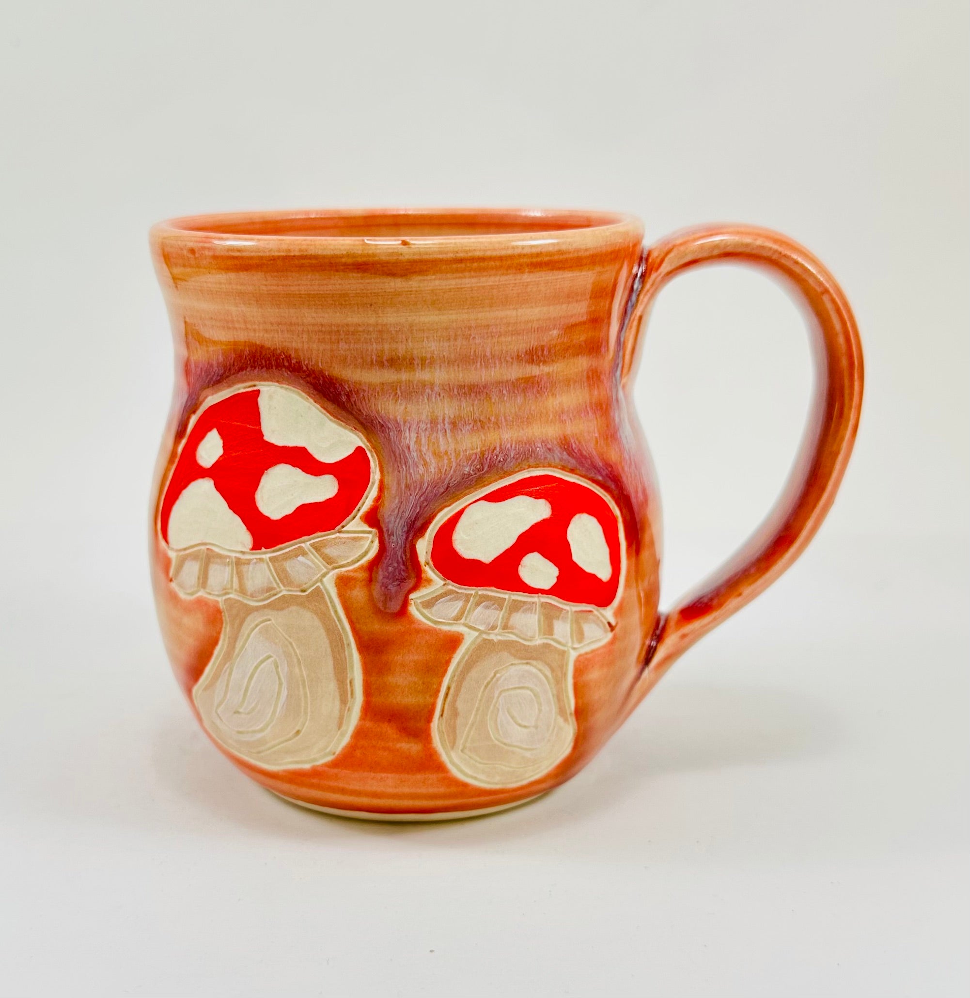 handmade ceramic mug in a beautiful peachy glaze with mushroom illustrations on it.