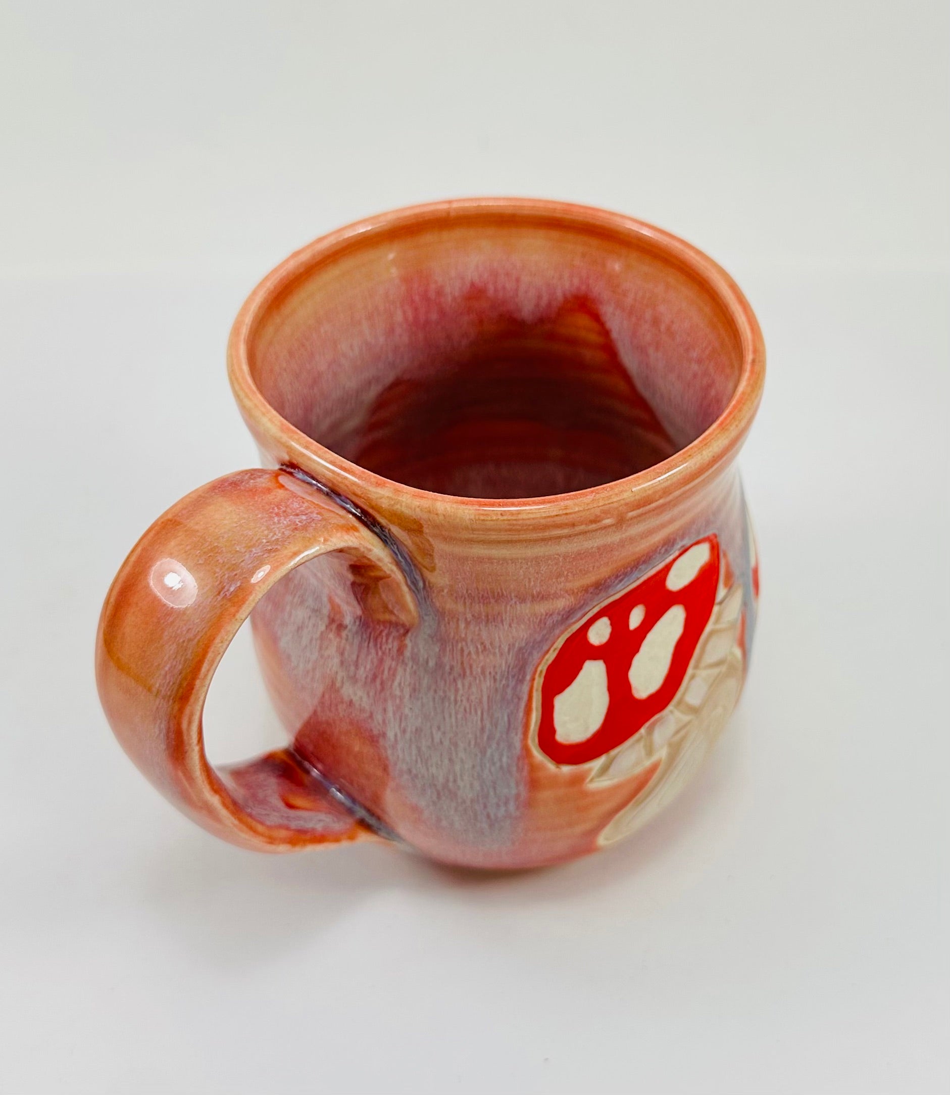 handmade ceramic mug in a beautiful peachy glaze with mushroom illustrations on it.