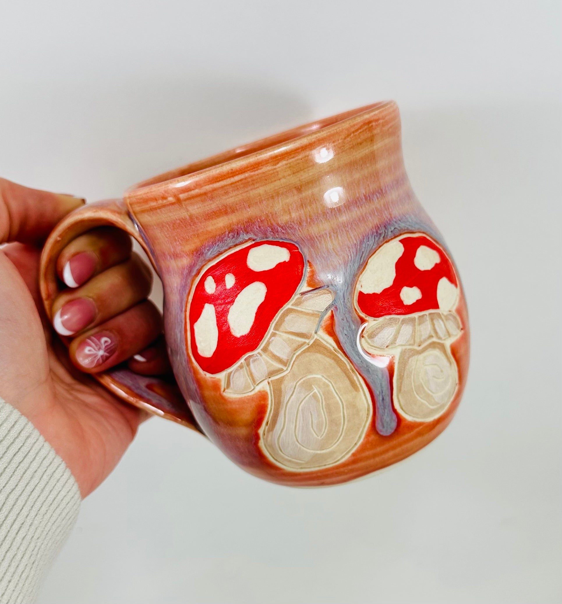 handmade ceramic mug in a beautiful peachy glaze with mushroom illustrations on it.