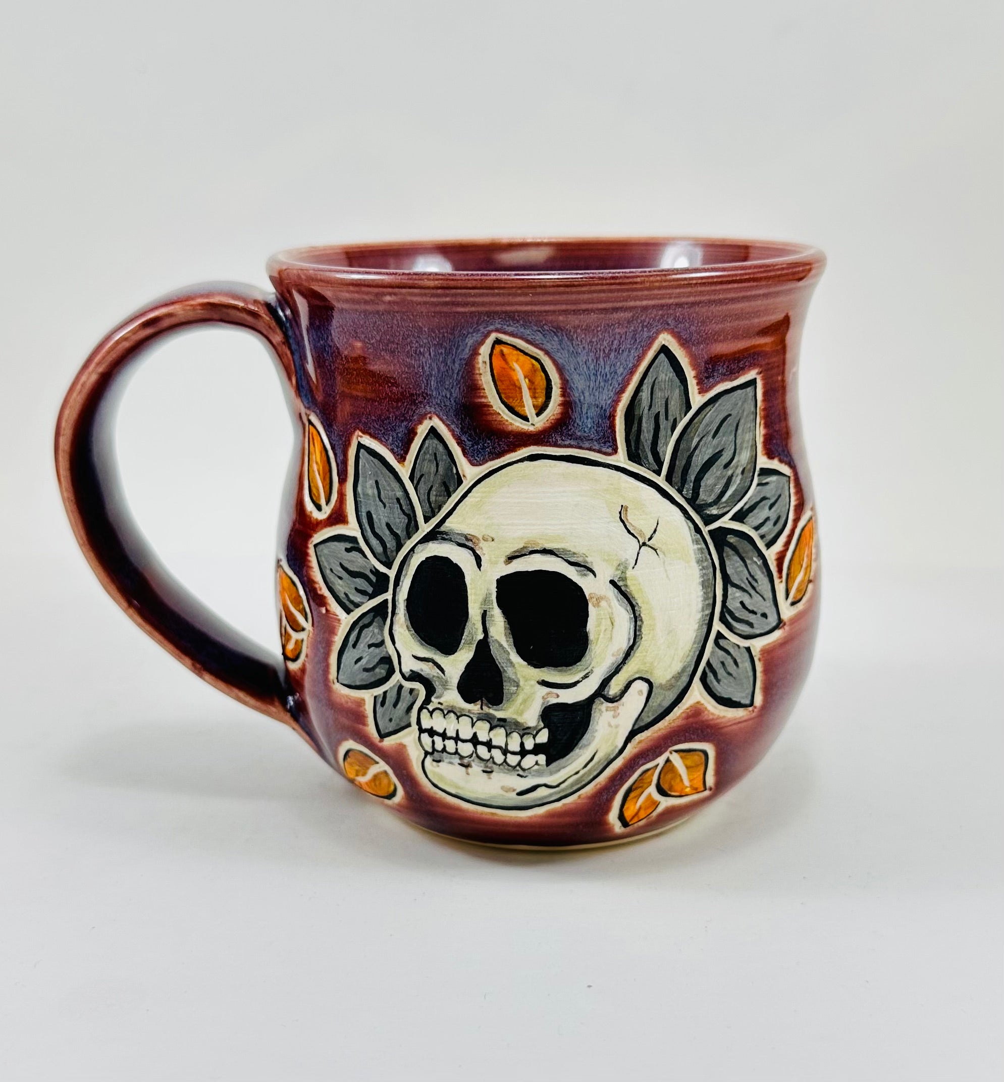 handmade ceramic mug in a beautiful purple glaze and a skull illustration on it.
