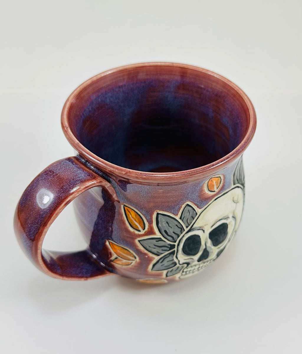 handmade ceramic mug in a beautiful purple glaze and a skull illustration on it.
