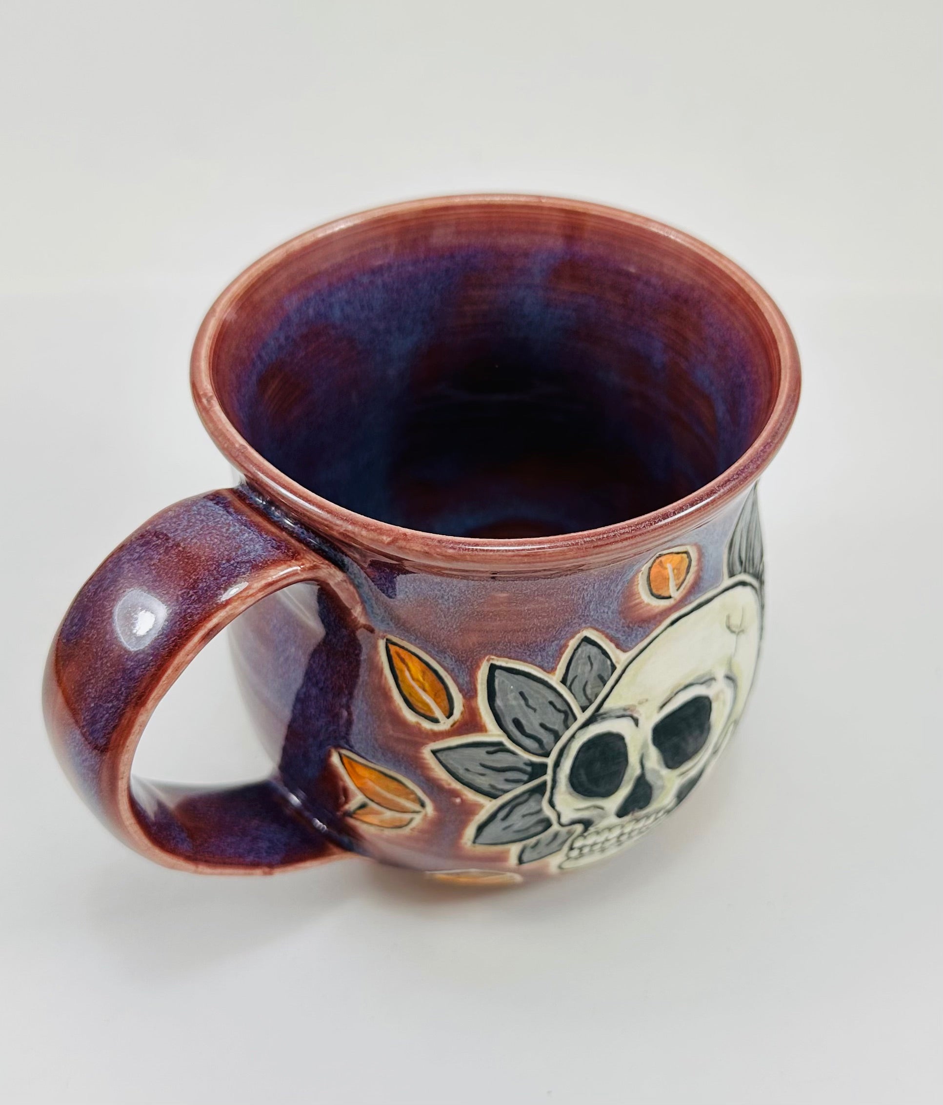 handmade ceramic mug in a beautiful purple glaze and a skull illustration on it.