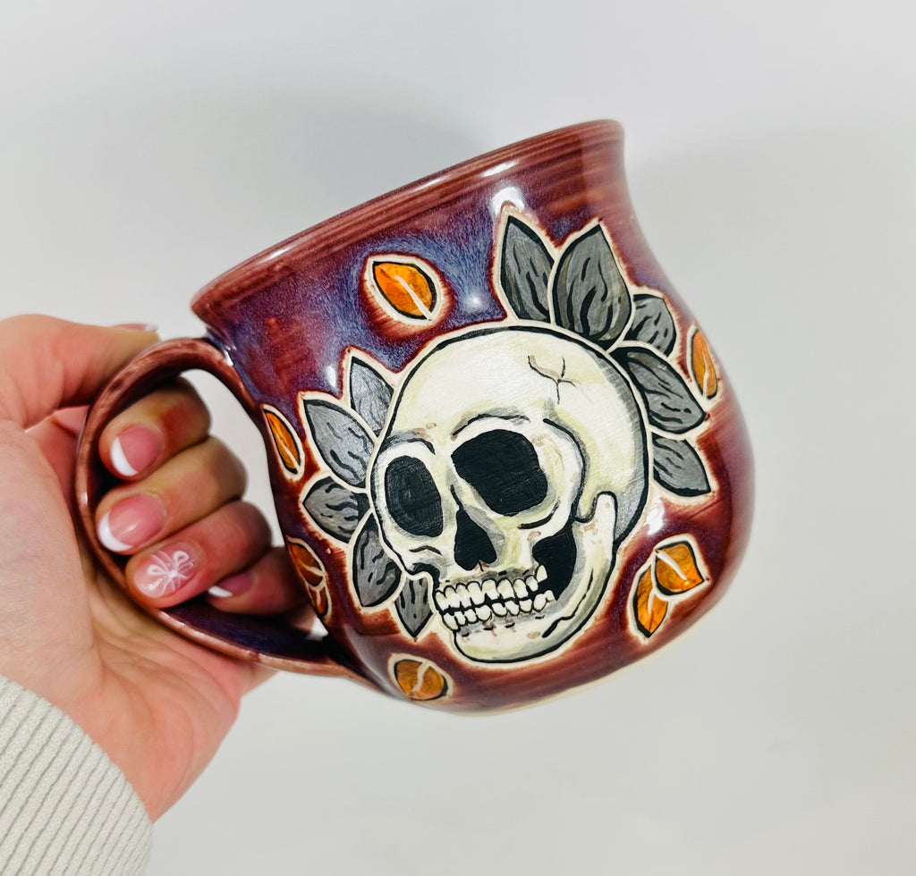 handmade ceramic mug in a beautiful purple glaze and a skull illustration on it.