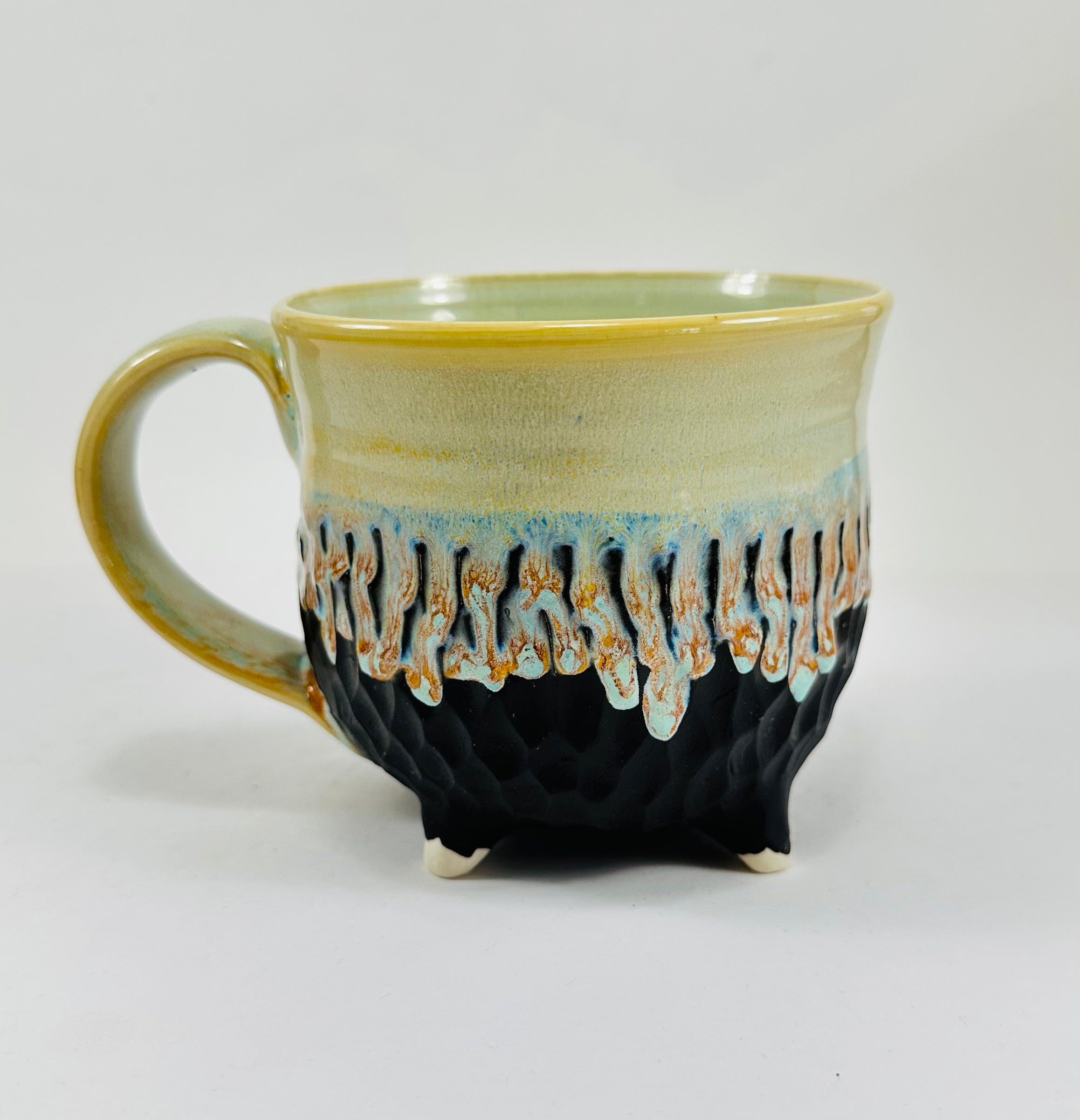 A handmade ceramic cauldron mug in a beautiful green and black glaze