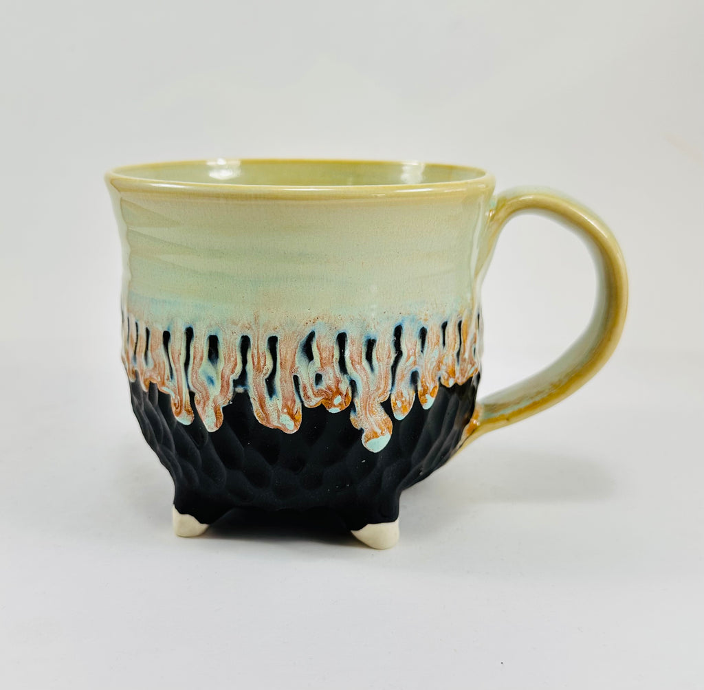 A handmade ceramic cauldron mug in a beautiful green and black glaze