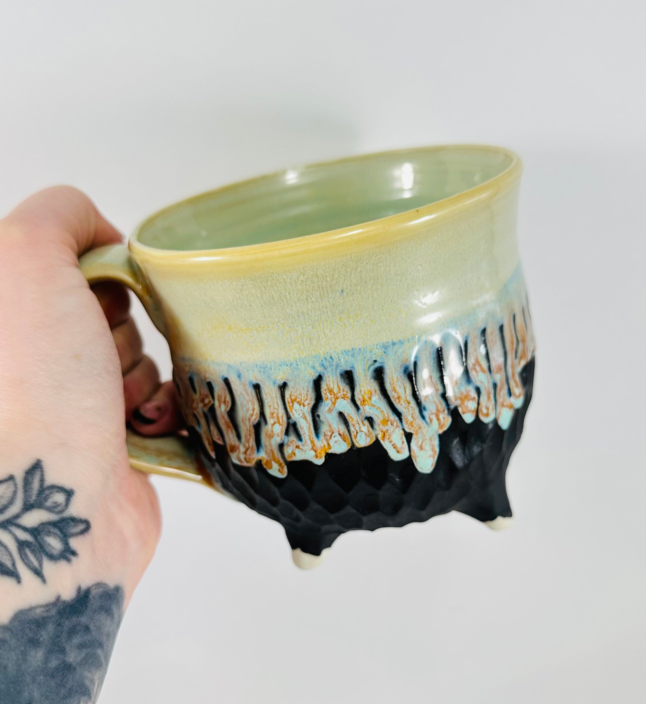 A handmade ceramic cauldron mug in a beautiful green and black glaze