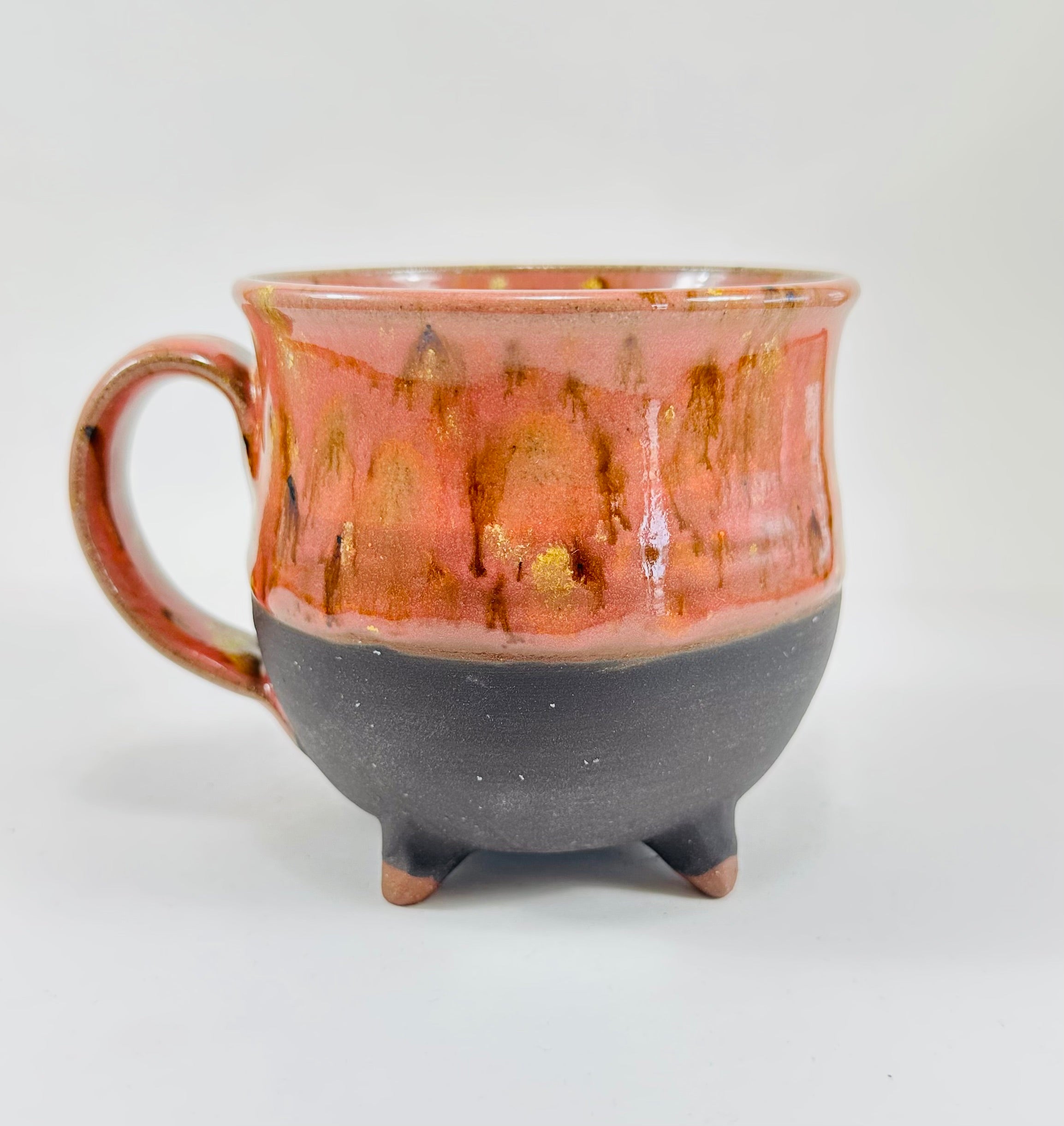 A handmade ceramic cauldron mug in a beautiful orange and black glaze