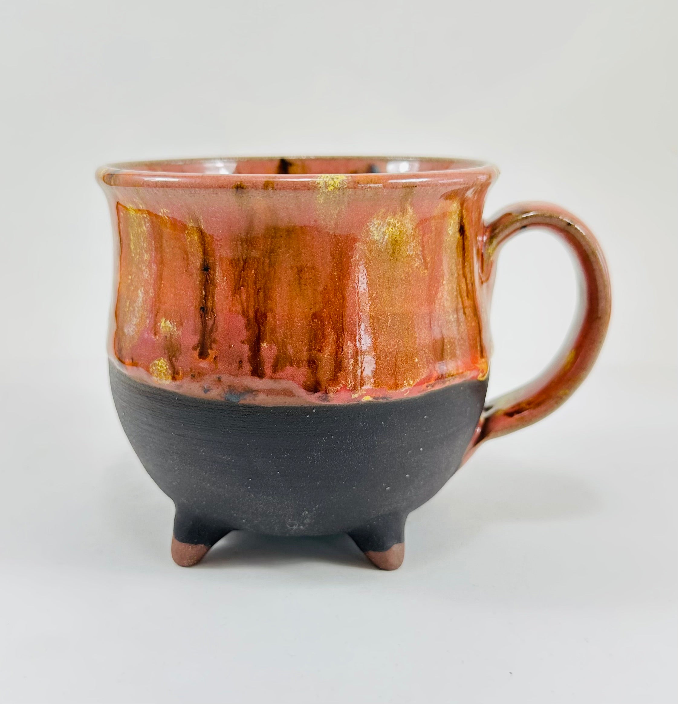 A handmade ceramic cauldron mug in a beautiful orange and black glaze