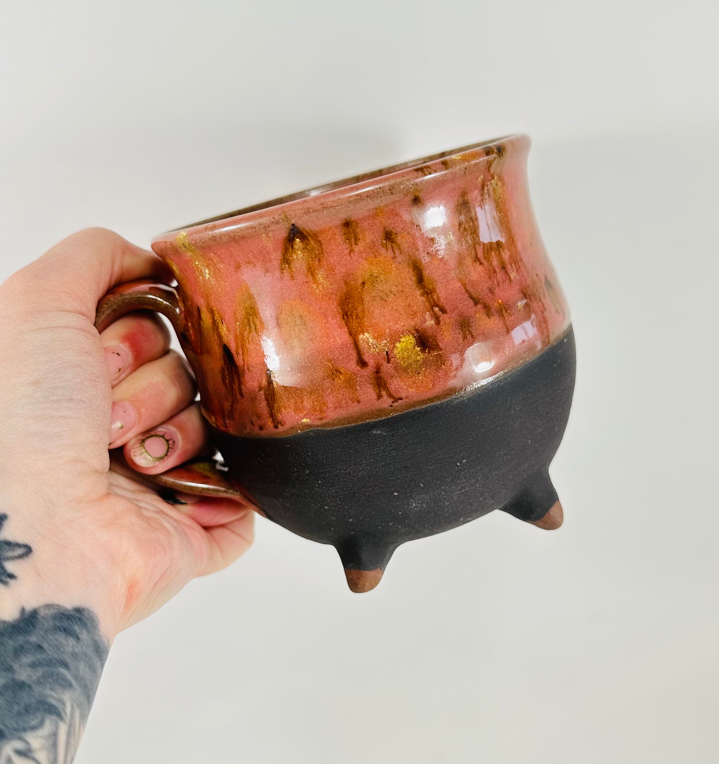 A handmade ceramic cauldron mug in a beautiful orange and black glaze