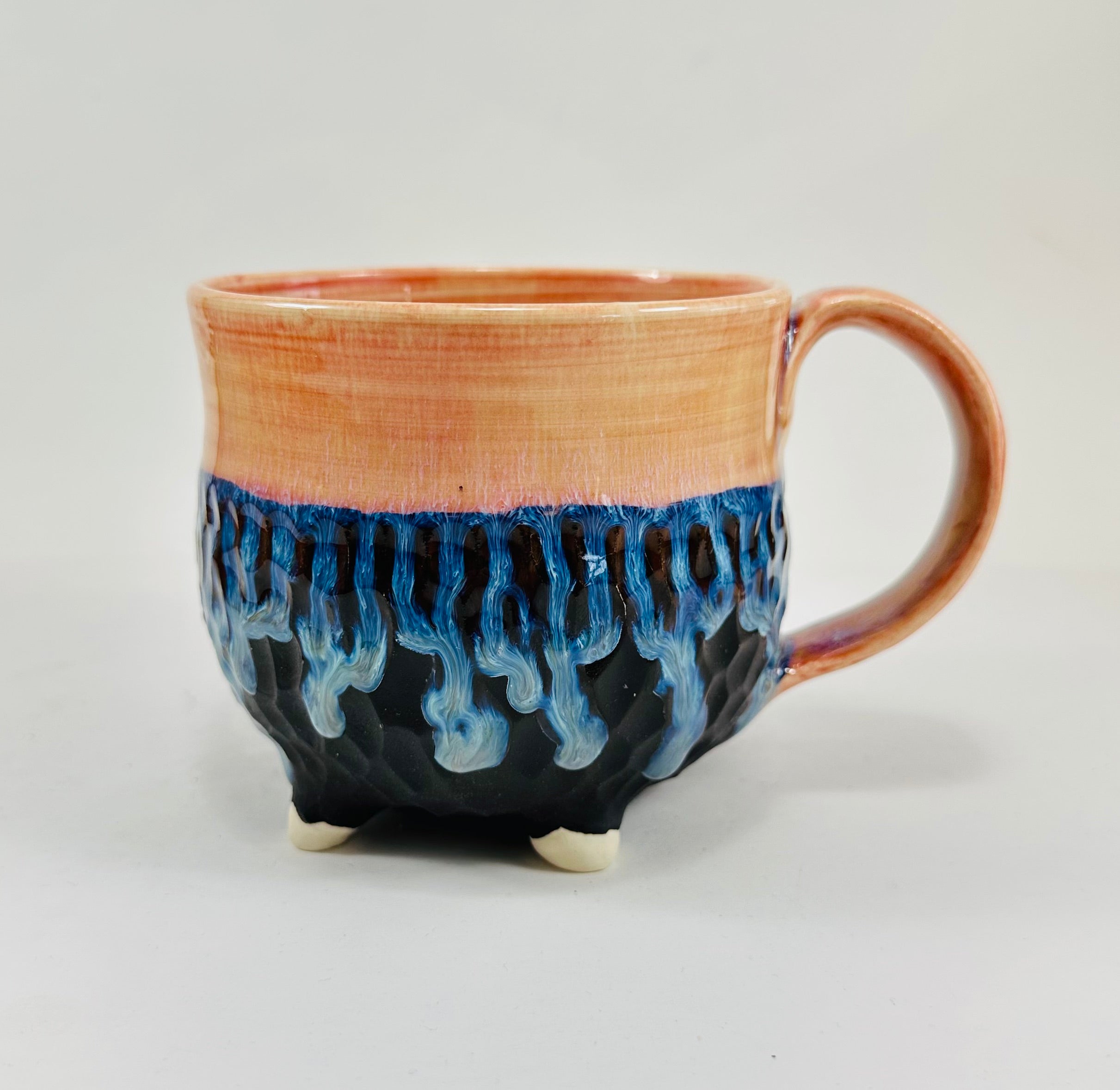 A handmade ceramic cauldron mug in a beautiful orange, blue  and black glaze