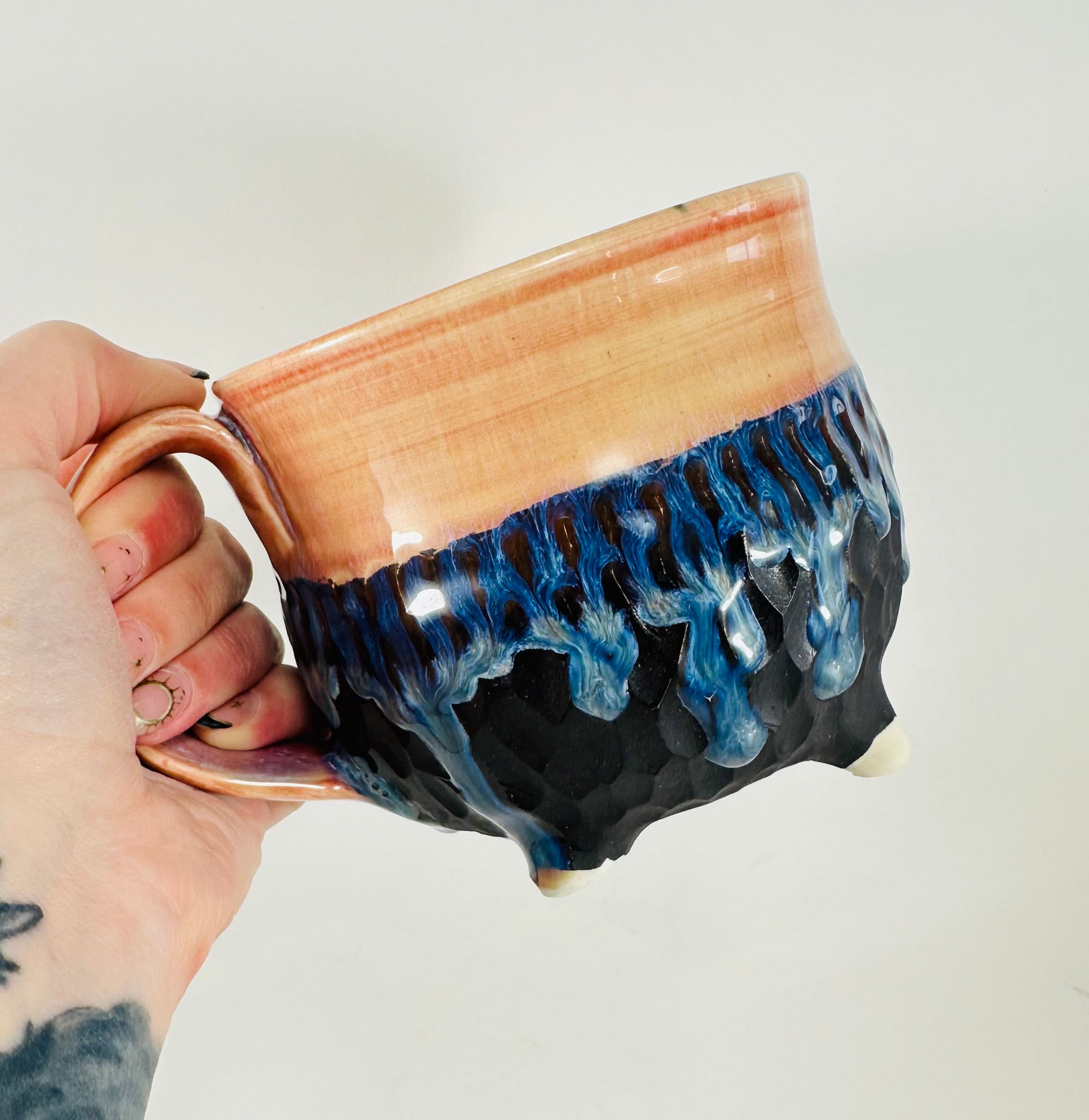 A handmade ceramic cauldron mug in a beautiful orange, blue  and black glaze