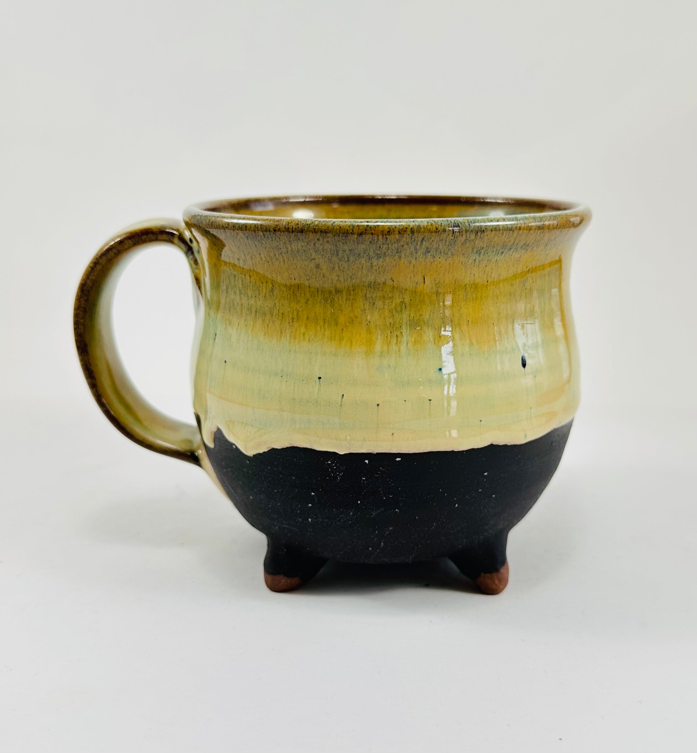 A handmade ceramic cauldron mug in a beautiful green and black glaze