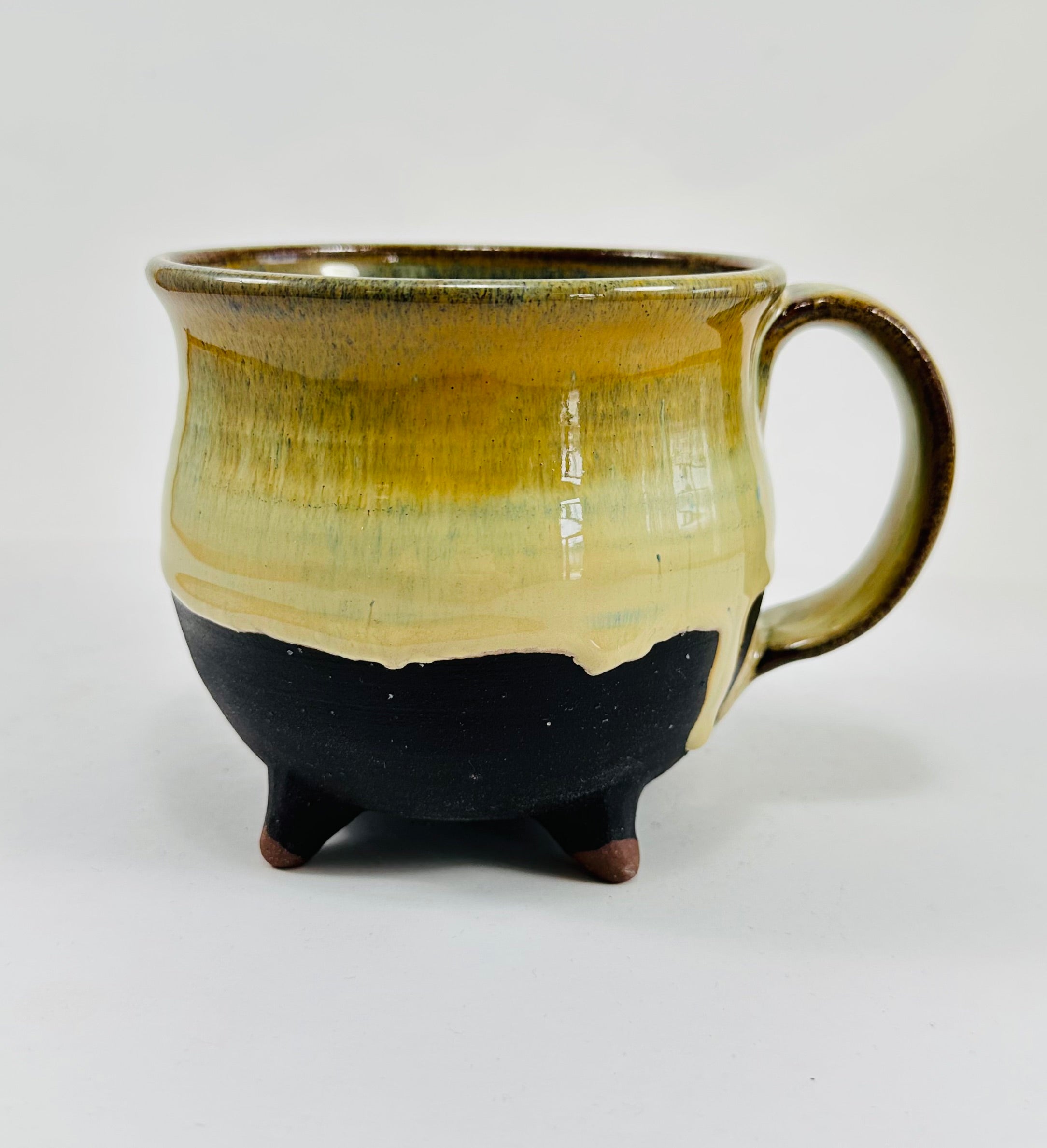 A handmade ceramic cauldron mug in a beautiful green and black glaze