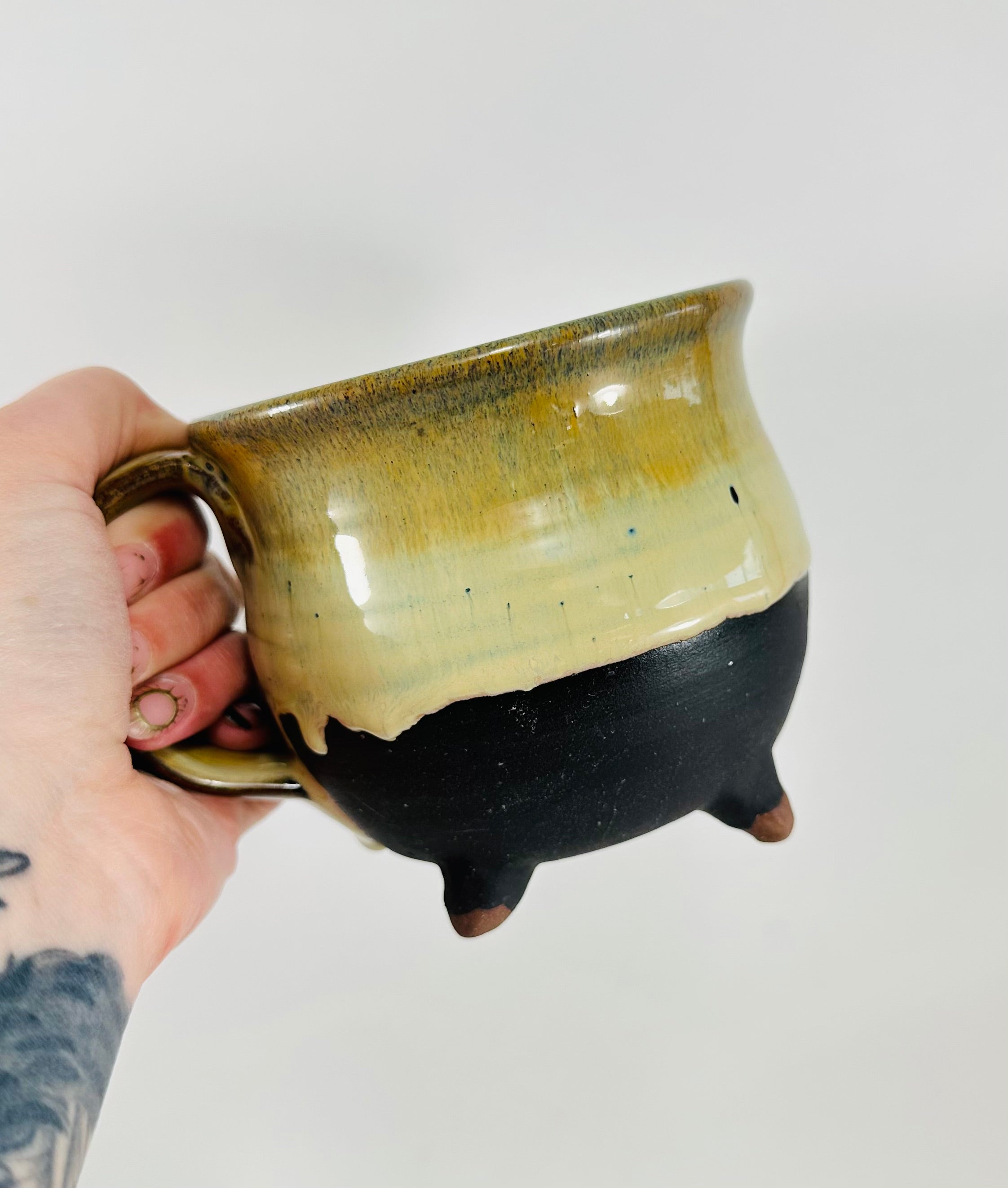 A handmade ceramic cauldron mug in a beautiful green and black glaze
