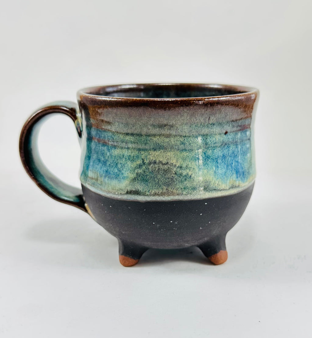A handmade ceramic cauldron mug in a beautiful green, blue, brown and black glaze