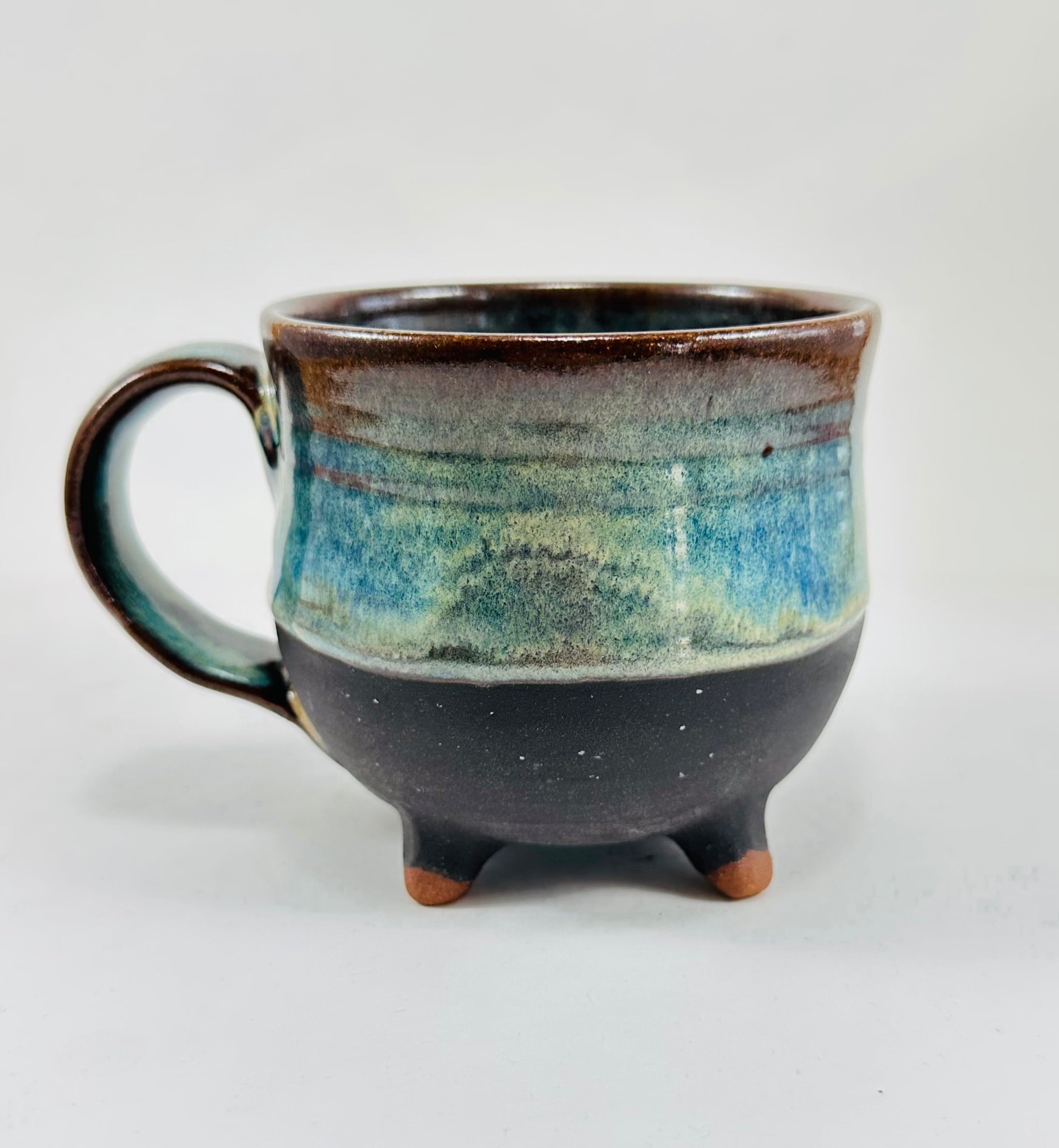 A handmade ceramic cauldron mug in a beautiful green, blue, brown and black glaze