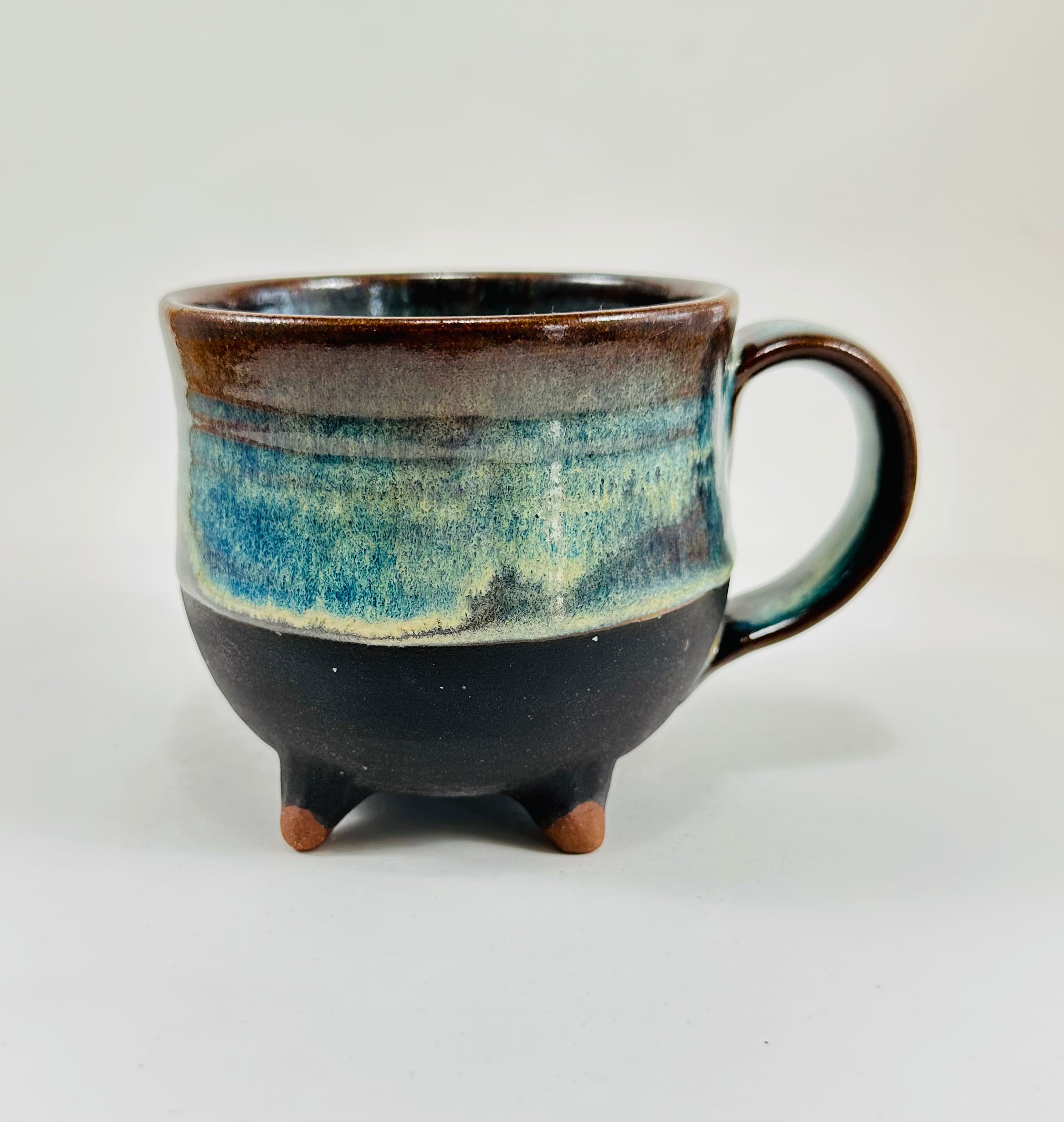 A handmade ceramic cauldron mug in a beautiful green, blue, brown and black glaze