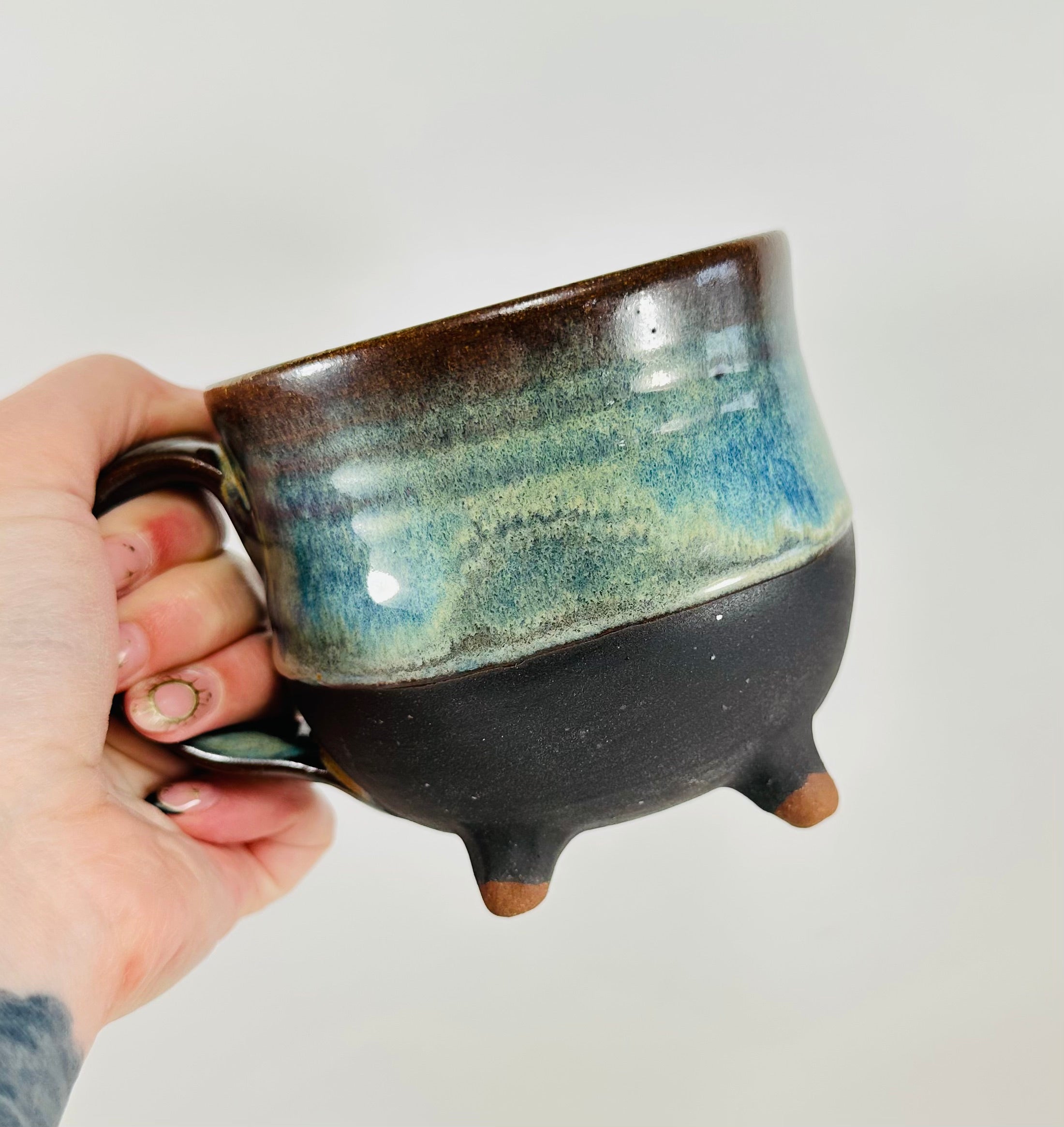 A handmade ceramic cauldron mug in a beautiful green, blue, brown and black glaze