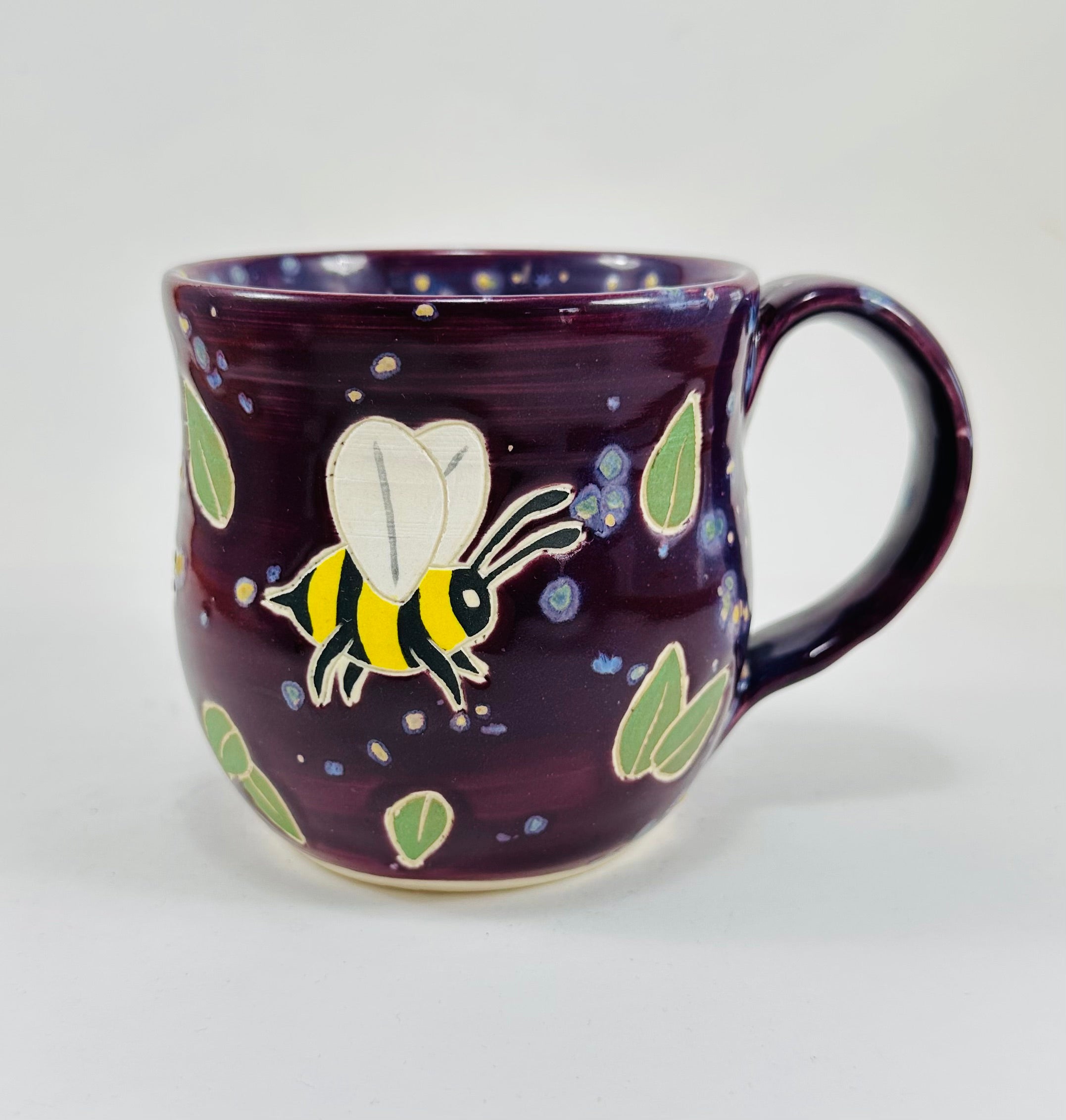 handmade ceramic mug in a beautiful purple glaze and bees illustrated on it.