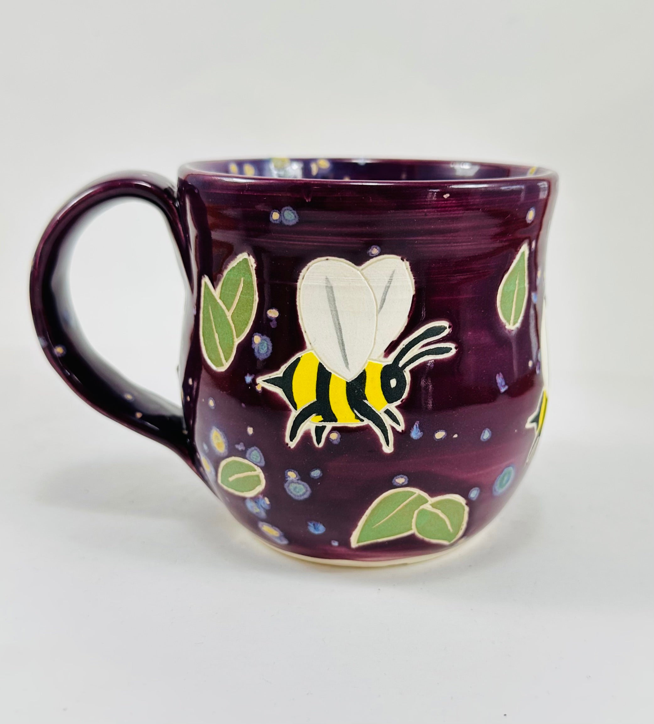 handmade ceramic mug in a beautiful purple glaze and bees illustrated on it.