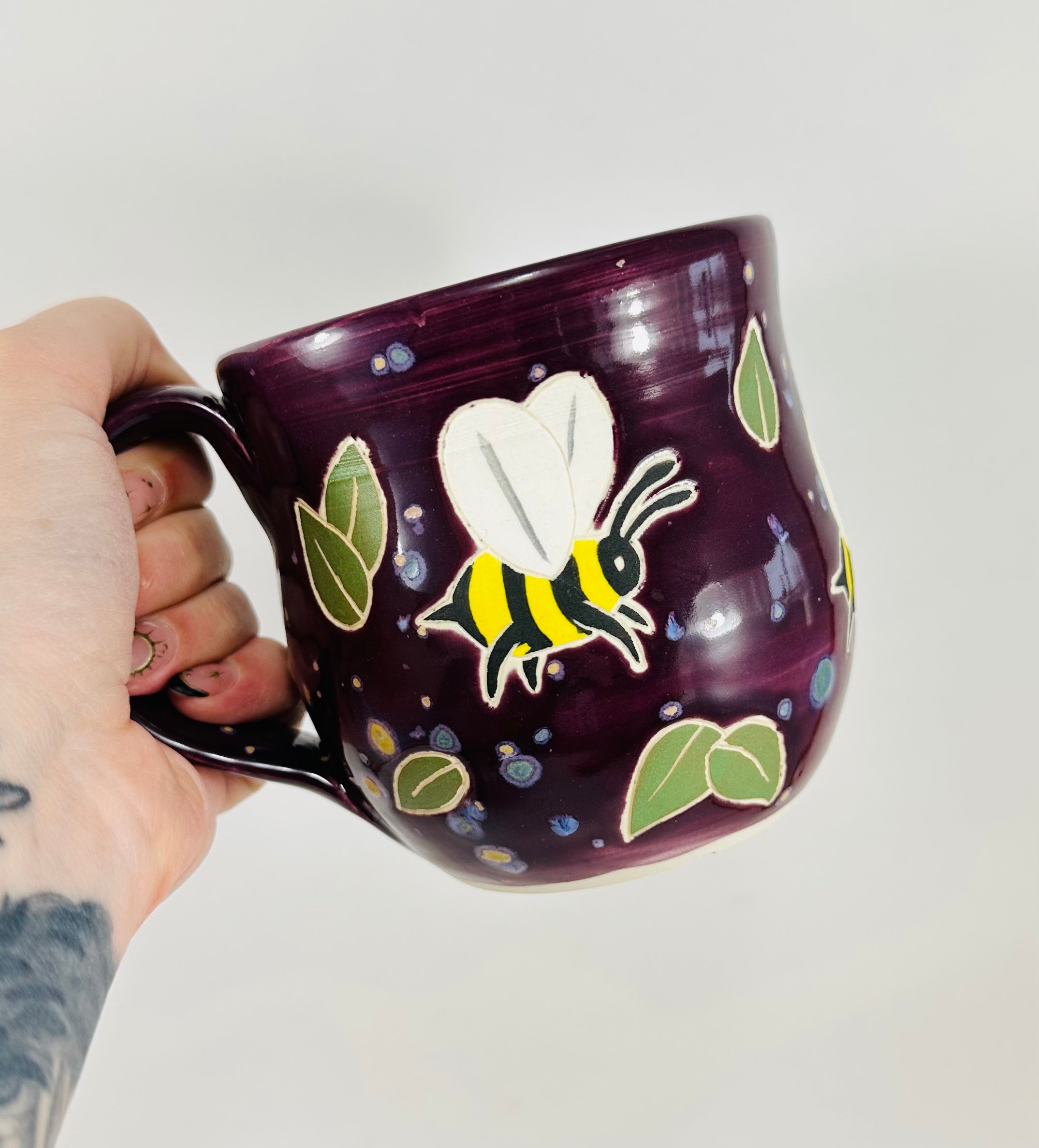 handmade ceramic mug in a beautiful purple glaze and bees illustrated on it.