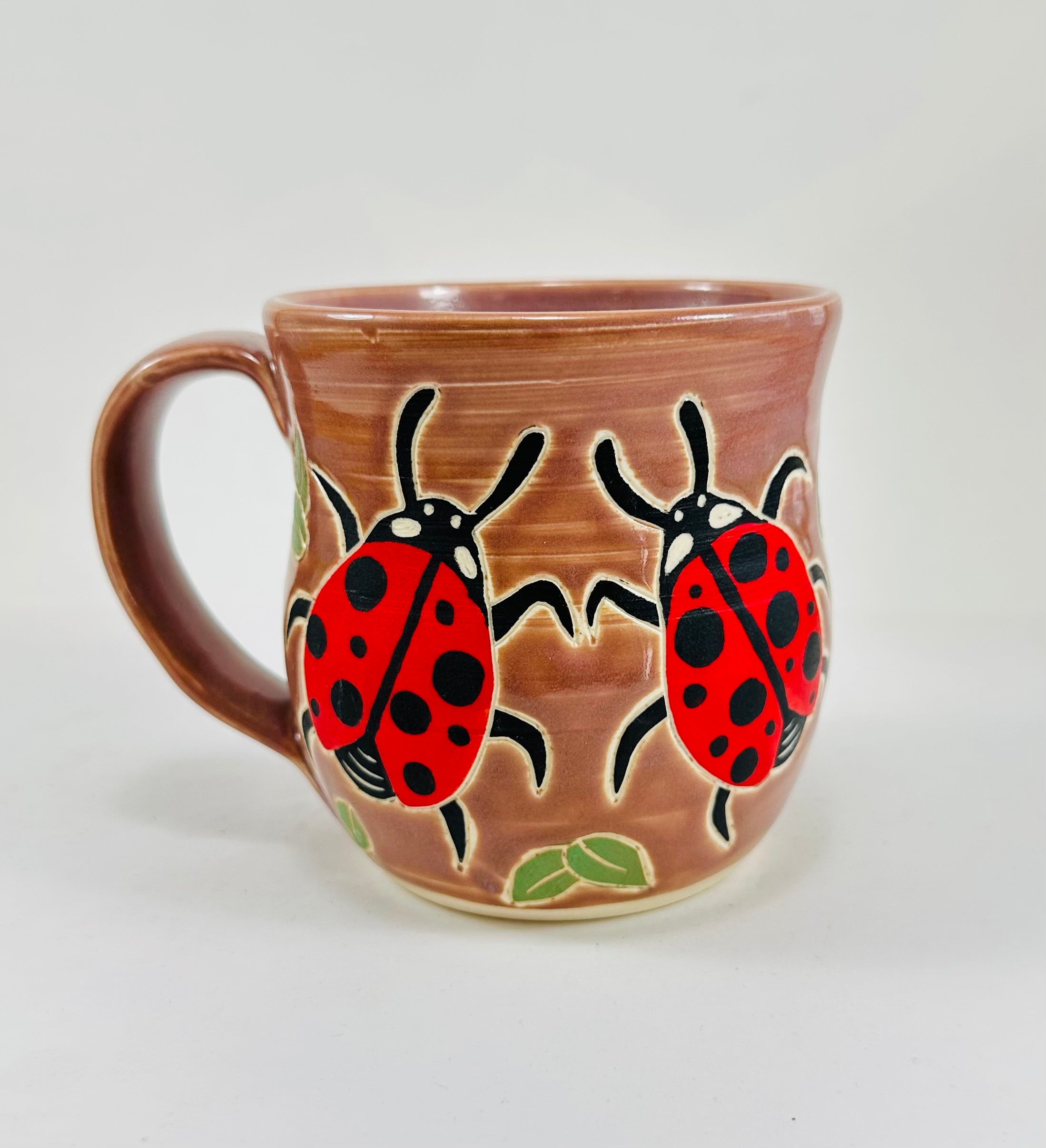 handmade ceramic mug in a beautiful lavender glaze and lady bugs illustrated on it.