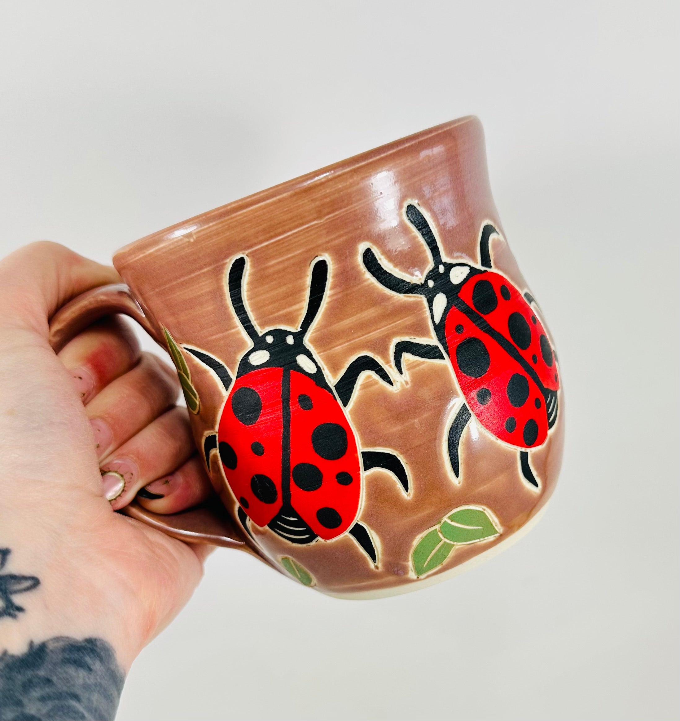handmade ceramic mug in a beautiful lavender glaze and lady bugs illustrated on it.