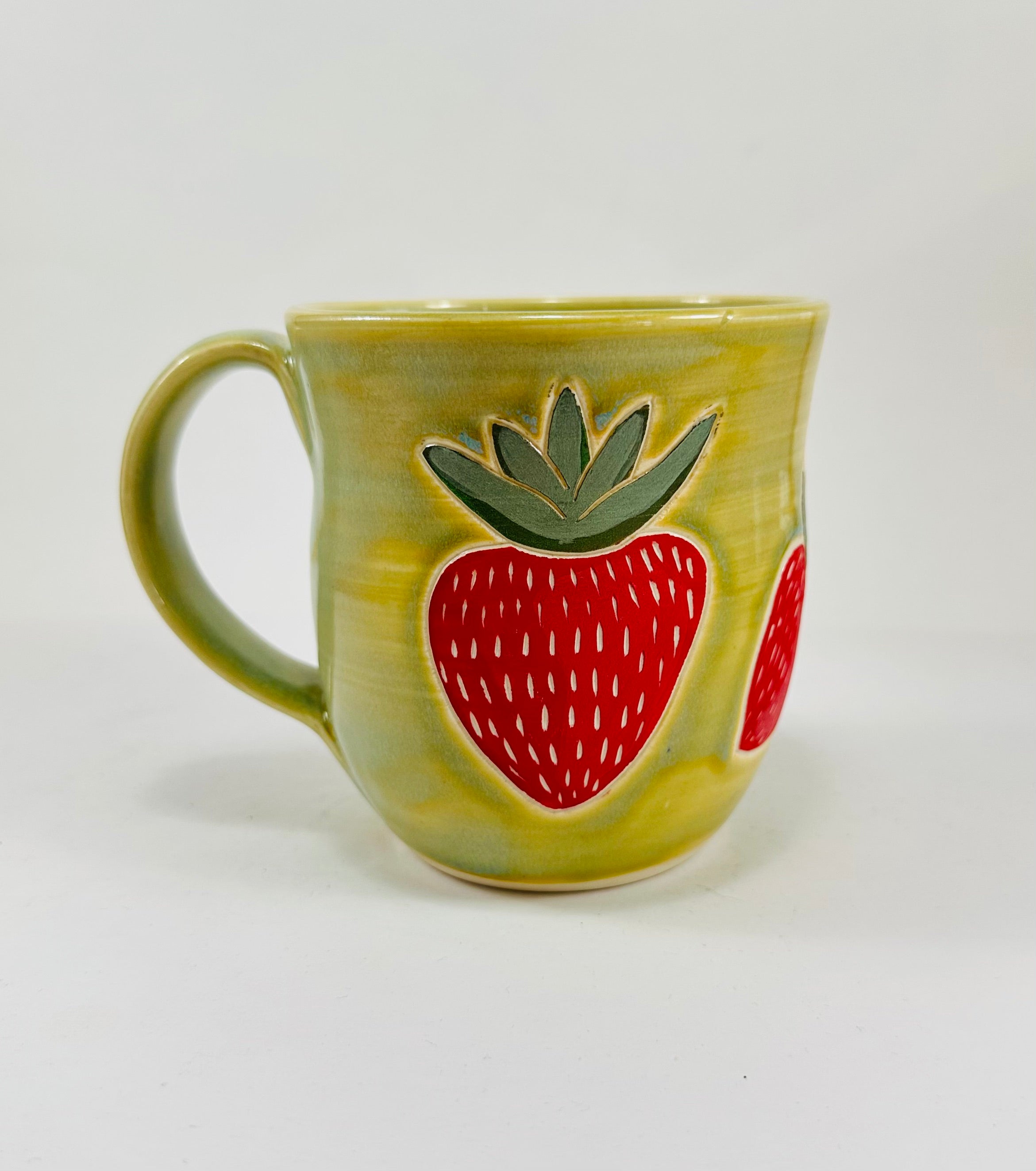 handmade ceramic mug in a beautiful green glaze with strawberries illustrated on it