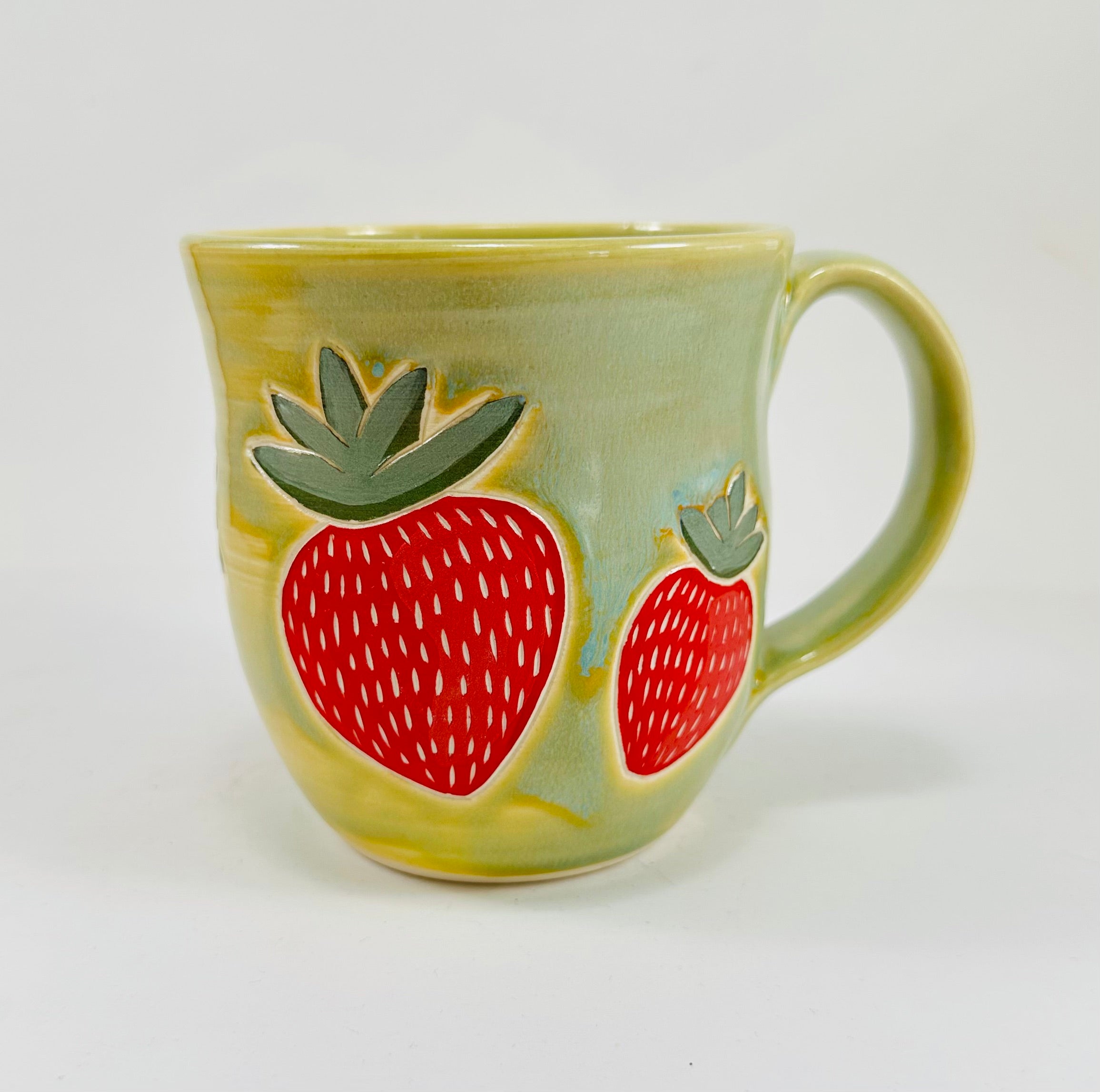 handmade ceramic mug in a beautiful green glaze with strawberries illustrated on it