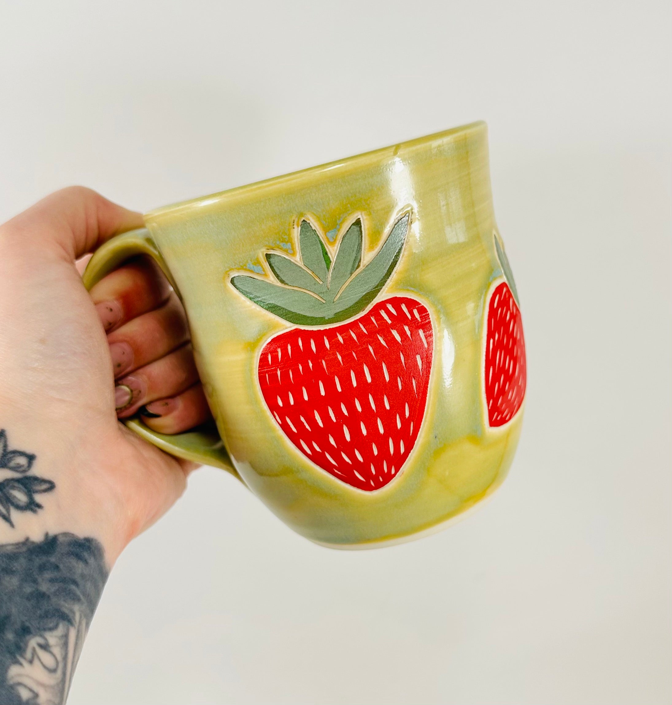 handmade ceramic mug in a beautiful green glaze with strawberries illustrated on it